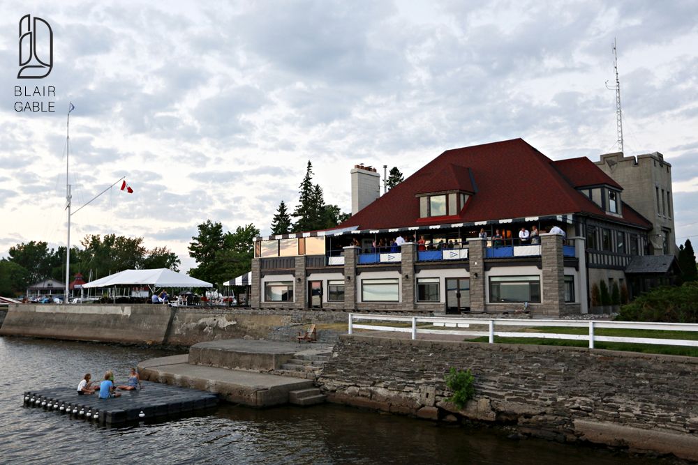 Exterior view from the water of the club house, docks and stone retaining wall, and the original stone tower.